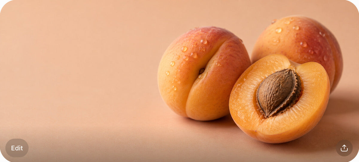 Two whole apricots and one halved apricot on a warm peach-colored surface