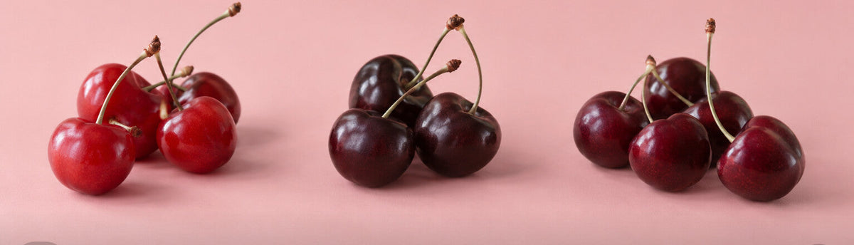 Three cherry clusters in bright red, near-black, and burgundy tones side by side on a blush surface