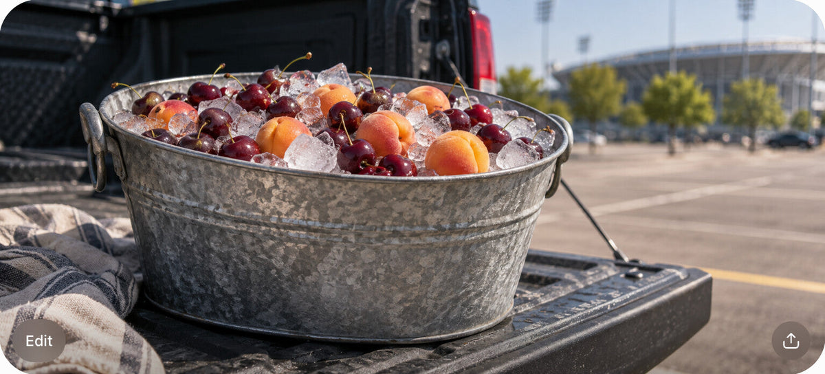 A galvanized ice tub with cherries and apricots on a pickup truck tailgate at a stadium parking lot